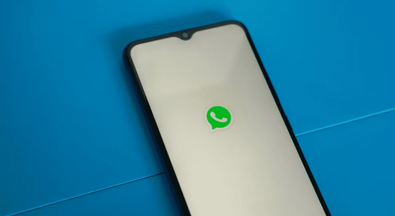  A white smartphone on a blue background with the WhatsApp logo on the screen, with a caption about tips to prevent WhatsApp status from being deleted.